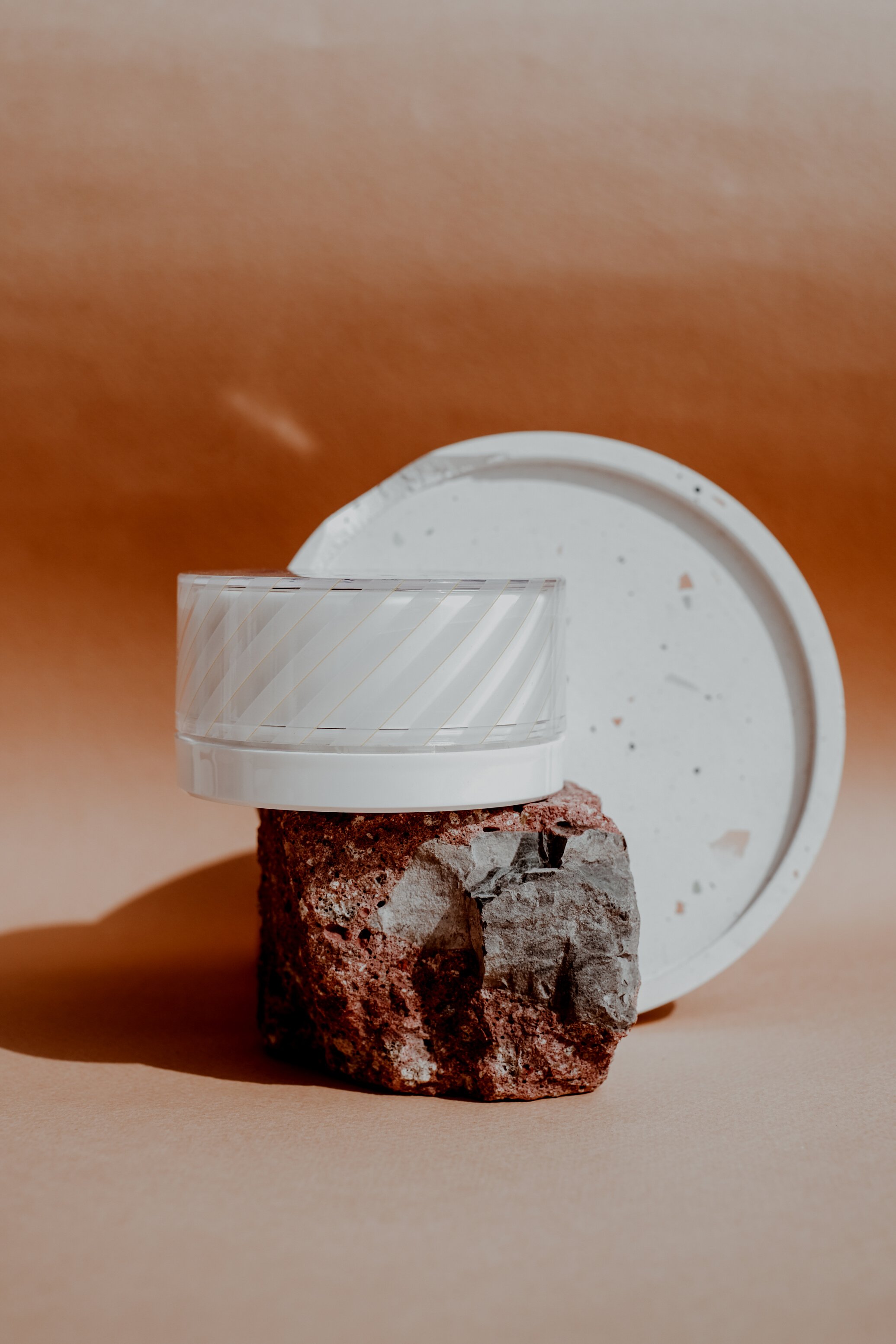 White Cosmetic Container on a Rock on Brown Background